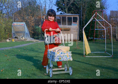 young girl in garden pushing dolls in a toy pram in the 1970s uk Stock Photo