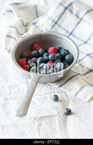Aluminum colander with fresh raspberries and blueberries over white textile background Stock Photo