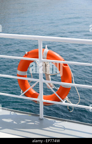 Orange colored lifebelt and rope hang on a white banister a passenger ship Stock Photo