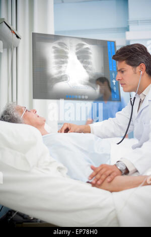 Doctor checking pulse of elderly patient beside screen displaying chest x-ray Stock Photo