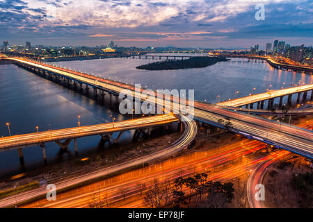 Traffic blurs across a bridge on the Han River as dusk settles in over Seoul, South Korea. Stock Photo