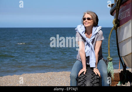 senior woman sitting by fishing boat on beach Stock Photo