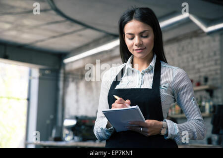 Happy beautiful female waiter in apron writing order Stock Photo