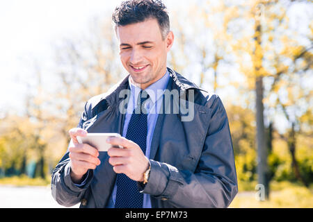 Happy businessman using smartphone in suit outdoors Stock Photo