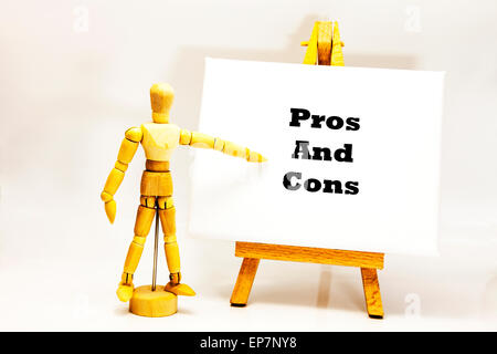 Wooden man with white board pointing at words 'Pros And Cons' for against list behalf of contrā contra The positive and negative Stock Photo