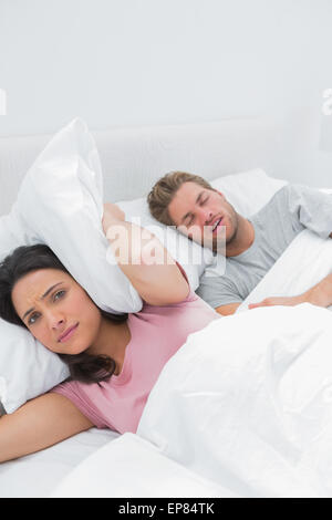 Upset woman covering ears with pillow next to husband snoring Stock Photo