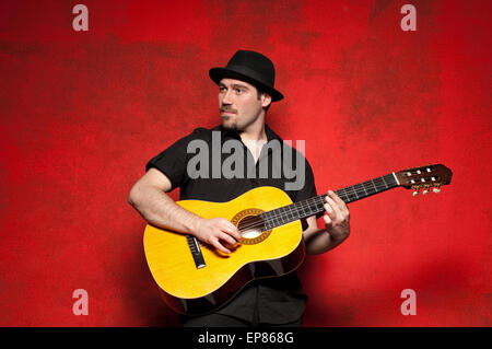 Young man playing guitar with joy on red background. Stock Photo