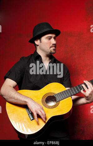 Young man playing guitar with joy on red background. Stock Photo