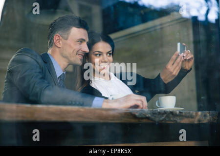 Smiling businesswoman and businessman making selfie photo on smartphone in cafe Stock Photo