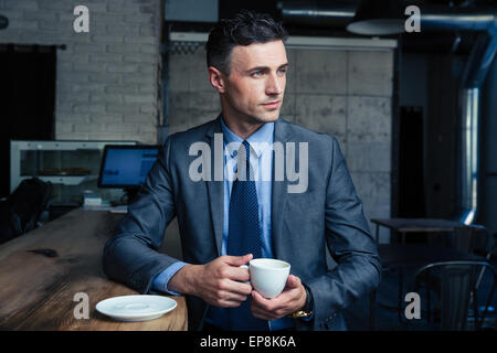 Thoughtful handsome businessman drinking coffee in cafe and looking away Stock Photo