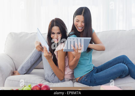 Friends sitting back to back showing each other their tablet pcs Stock Photo