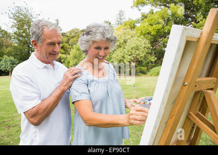 Content retired woman painting on canvas and talking with husband Stock Photo