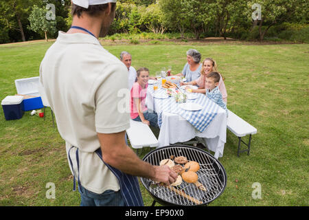 Father in chefs hat and apron cooking barbecue for his family Stock Photo
