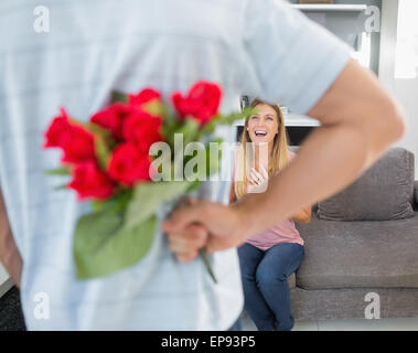 Man hiding bouquet of roses from smiling girlfriend on the couch Stock Photo