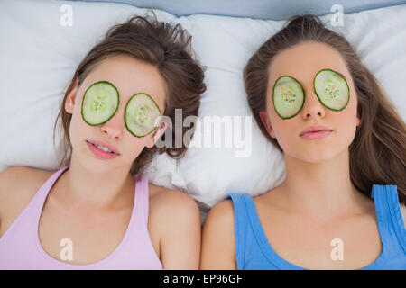 Friends lying in bed with cucumber slices on eyes Stock Photo