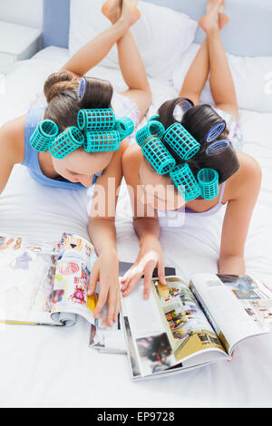 Girls in hair rollers lying in bed and reading Stock Photo