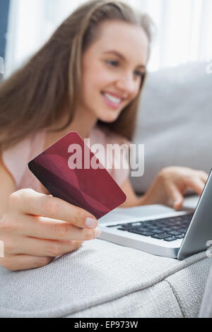 Smiling woman lying ona sofa holding a card and laptop Stock Photo