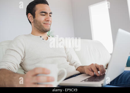 Peaceful handsome man having coffee while using his laptop Stock Photo