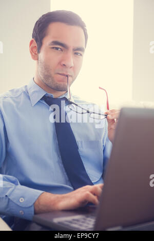 Irritated man biting his eyeglasses and using a laptop Stock Photo