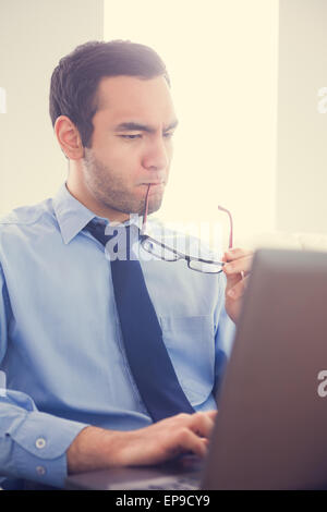 Focused man biting his eyeglasses and using a laptop Stock Photo