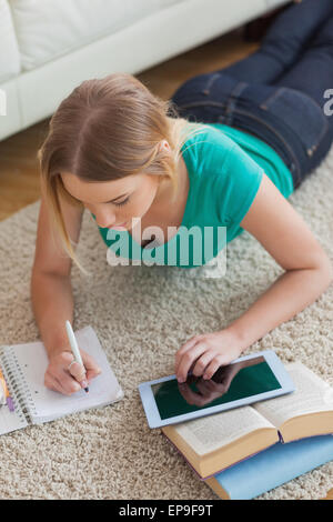 Focused young woman lying on floor using tablet to do her assignment Stock Photo