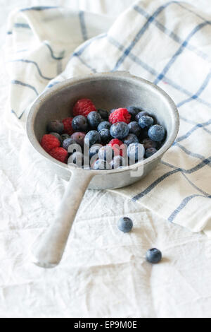 Aluminum colander with fresh raspberries and blueberries over white textile background Stock Photo