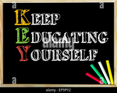 Acronym KEY as KEEP EDUCATING YOURSELF. Written note on wooden frame blackboard, colored chalk in the corner. Motivational Concept image Stock Photo