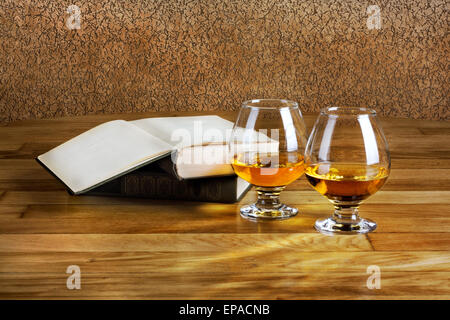 Two goblets of brandy and open book on wooden old counter top Stock Photo