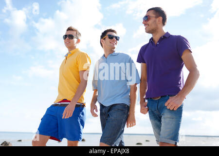 smiling friends in sunglasses walking along beach Stock Photo