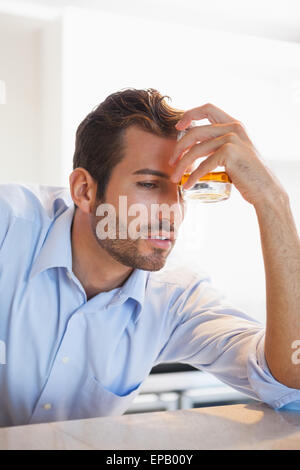 Drunk businessman clutching whiskey glass to forehead Stock Photo