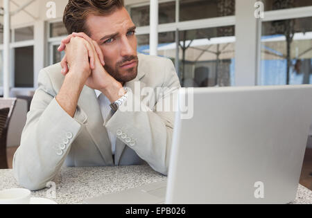 Frowning businessman looking at his laptop at table having coffee Stock Photo