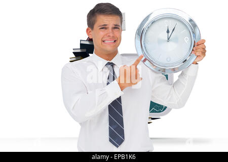 Composite image of anxious businessman holding and showing a clock Stock Photo