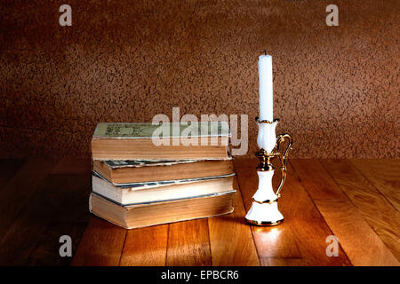 Old stack of books with candlestick and burning candle on the wooden table Stock Photo