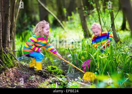 Children playing outdoors. Two preschooler kids catching frog with colorful net. Little boy and girl fishing in a forest river Stock Photo