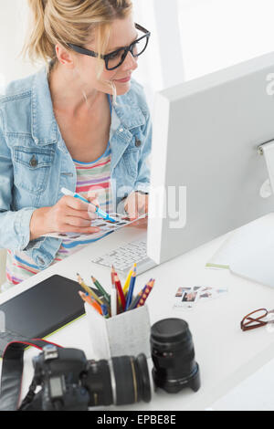 Blonde photographer looking over contact sheet at desk Stock Photo