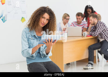 Happy designer sitting in front of her colleagues using digital tablet Stock Photo