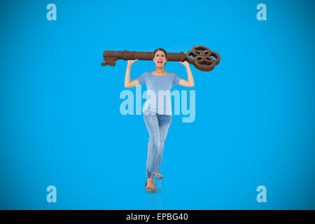 Composite image of annoyed brunette carrying large key Stock Photo