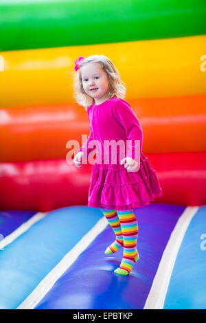 Cute funny preschool little girl playing, jumping and bouncing in an inflatable castle at birthday party on a kids playground Stock Photo