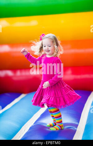 Cute funny preschool little girl playing, jumping and bouncing in an inflatable castle at birthday party on a kids playground Stock Photo