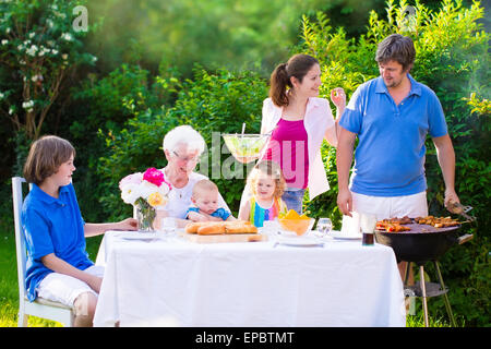 Grill barbecue backyard party. Happy big family enjoying BBQ lunch with grandmother eating grilled meat in the garden with salad Stock Photo