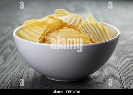 rippled organic chips in white bowl on wooden table Stock Photo