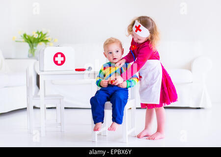 Two happy children, cute toddler girl and baby boy, brother and sister, playing doctor and hospital using stethoscope toy Stock Photo