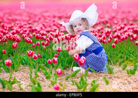 Adorable curly toddler girl wearing Dutch traditional national costume dress in a field of blooming tulips next to windmill Stock Photo