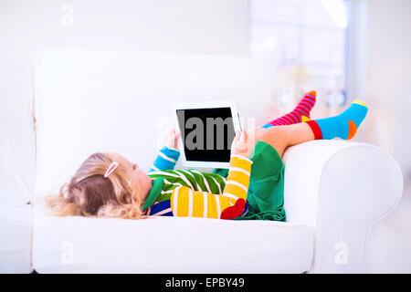Funny little toddler girl with tablet pc relaxing on a white couch Stock Photo