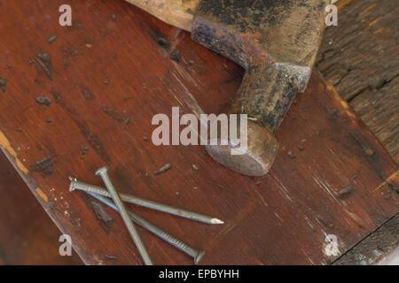 Old and worn contracting hammer and three nails on a distressed work bench Stock Photo