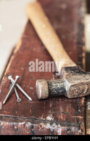 Old and worn contracting hammer and three nails on a distressed work bench Stock Photo