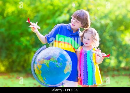 Two happy children, cute curly toddler girl and a smiling school age boy playing with toy airplanes flying over the globe Stock Photo