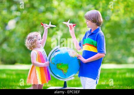 Two happy children, cute curly toddler girl and a smiling school age boy playing with toy airplanes flying over the globe Stock Photo