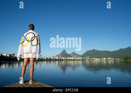 RIO DE JANEIRO, BRAZIL - MARCH 04, 2015: Man stands draped in Olympic flag in front of a skyline view at Lagoa de Freitas Lagoon Stock Photo