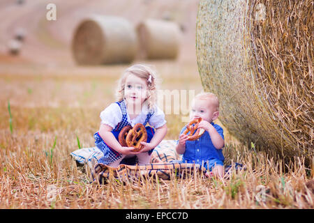 Two children, funny curly toddler girl and a little baby boy, wearing traditional German costumes playing in a field Stock Photo
